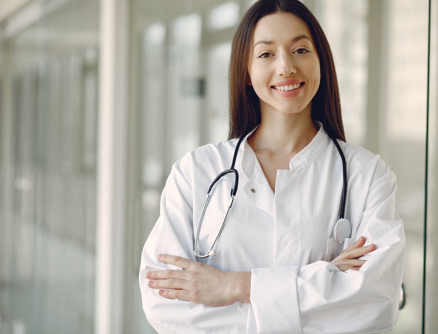 A smiling healthcare professional in a white coat with a stethoscope, arms crossed