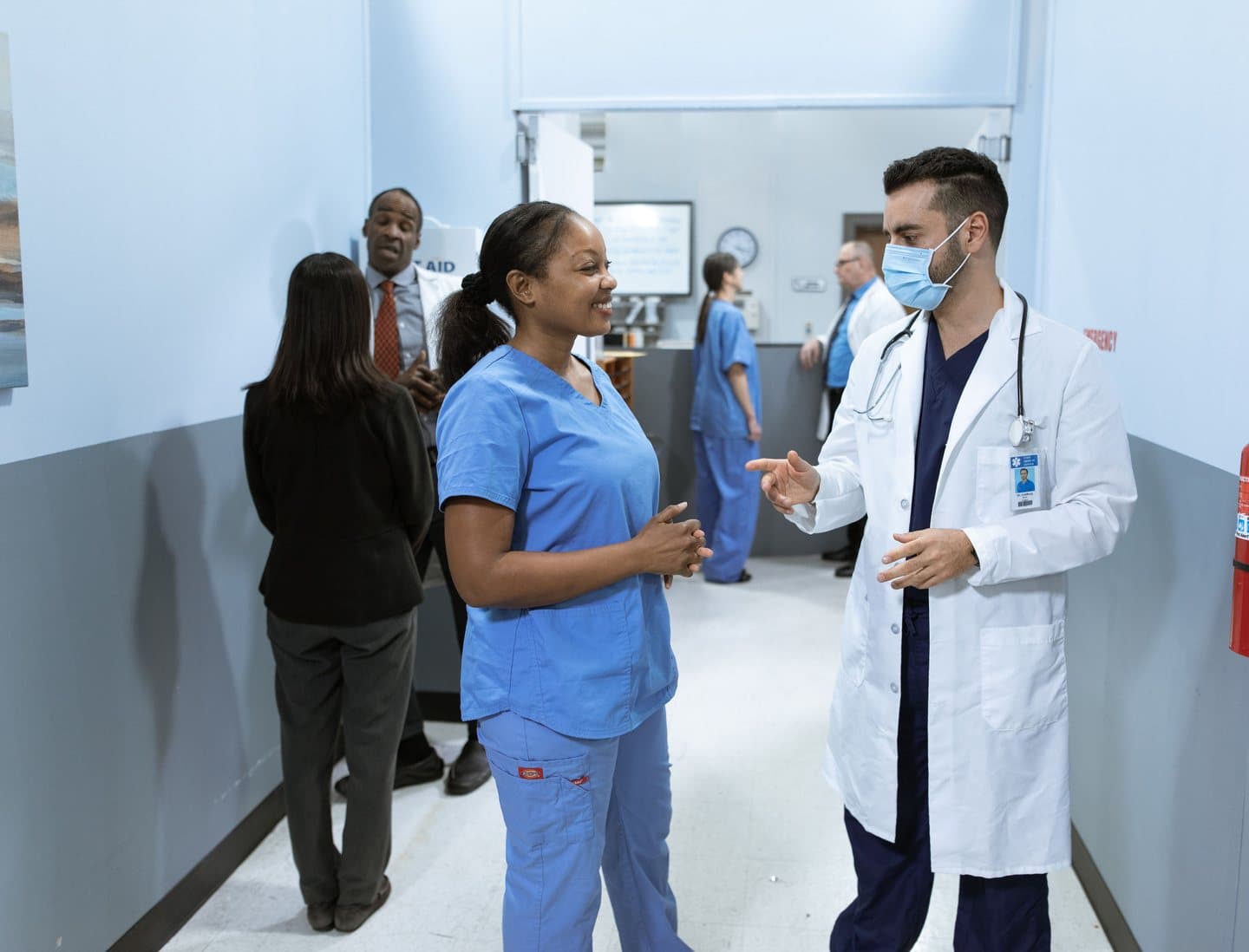 A nurse in blue scrubs talking with a doctor in a hospital corridor