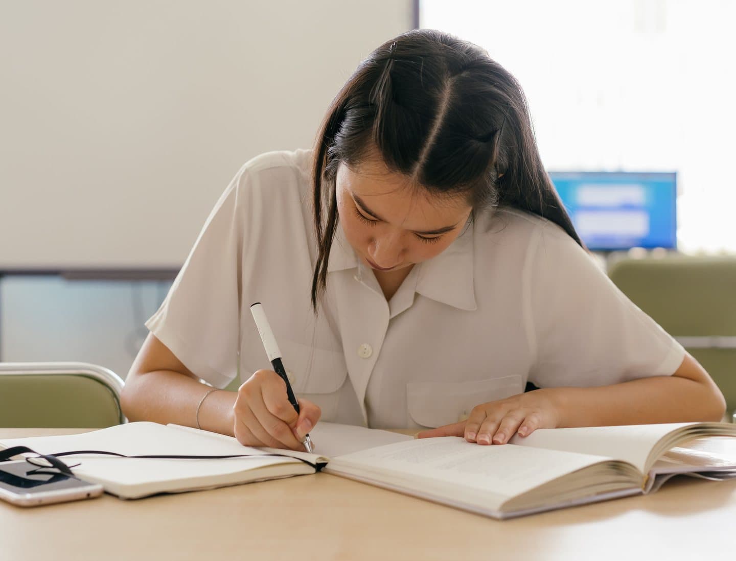 A student writing notes from an open book while studying at a desk
